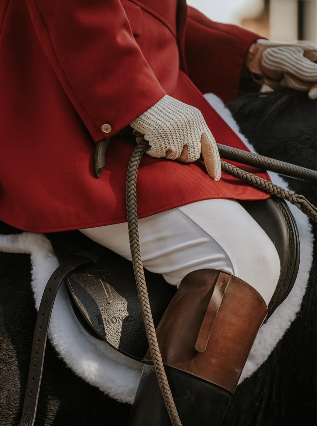 Detail of a scarlet hunt coat, braided rein, and riding boot